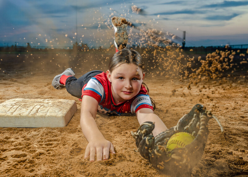 A young teen catches the softball right before it hits the ground throwing dust up. 