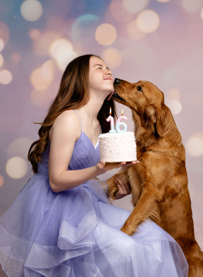 16th birthday photos of girl holding cake and her dog licking her face. Studio photo session was taken at Family Photo Studio near Atlanta, GA.