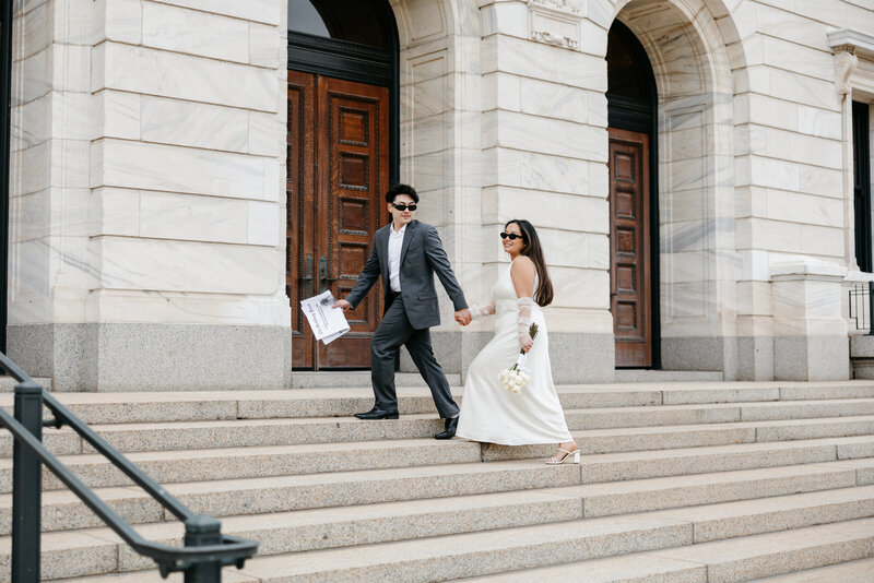 Bride and groom wearing sunglasses and holding hands while they walk up courthouse steps