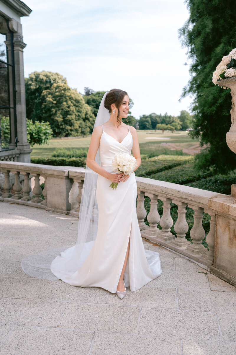 Lachende bruid met wit trouwboeket in hand poseert bij kasteel