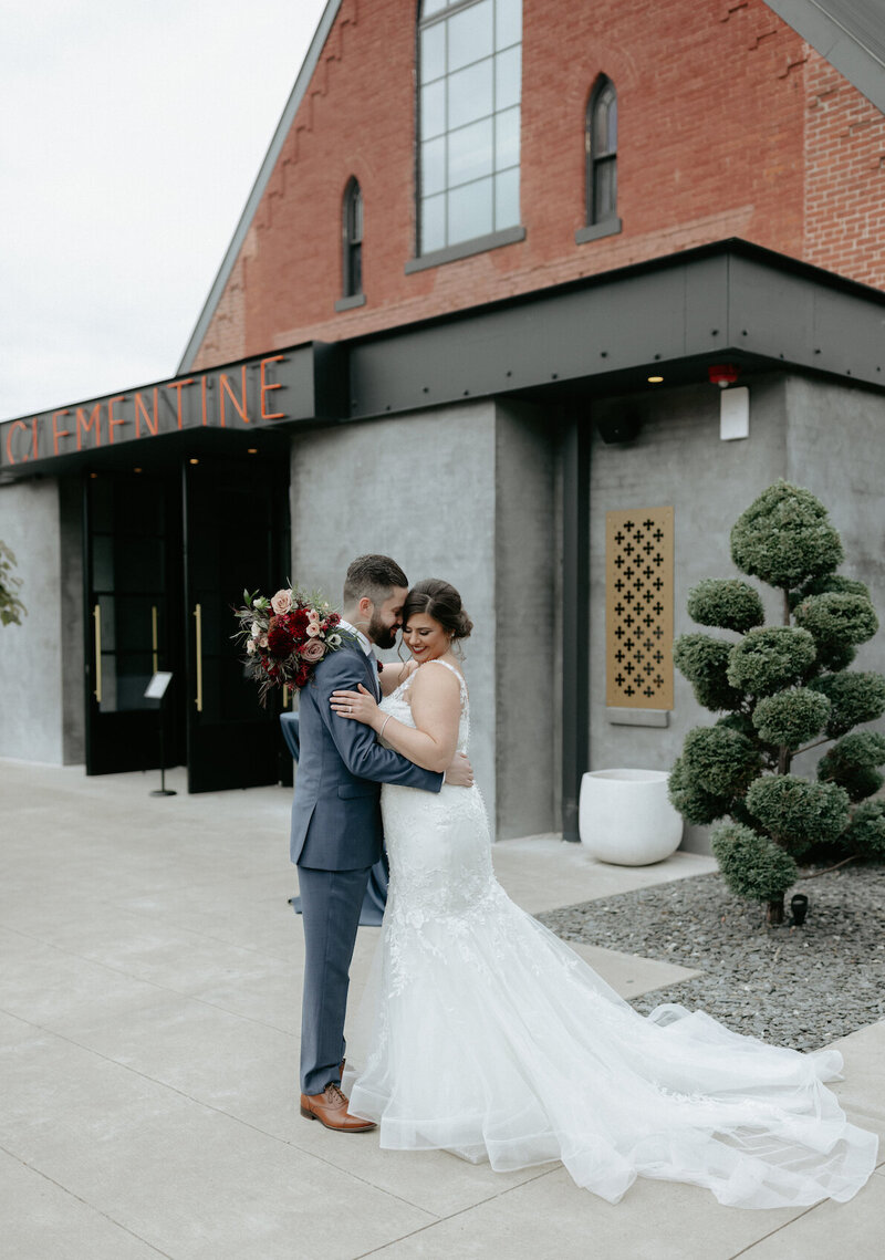 A couple holding onto one another outside their wedding venue.