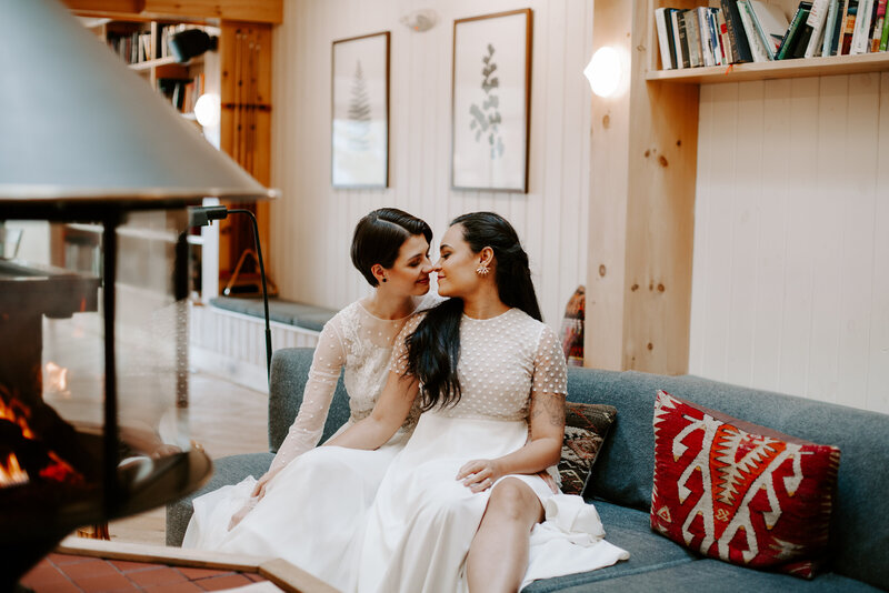 Two brides sitting on a couch about to kiss