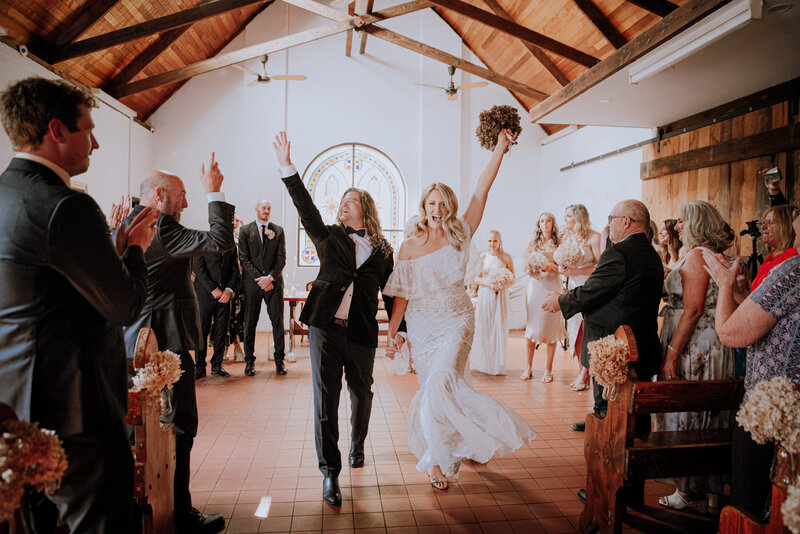 Bride & Groom celebrating with their hands in the air as they make their way up the aisle inside a chapel