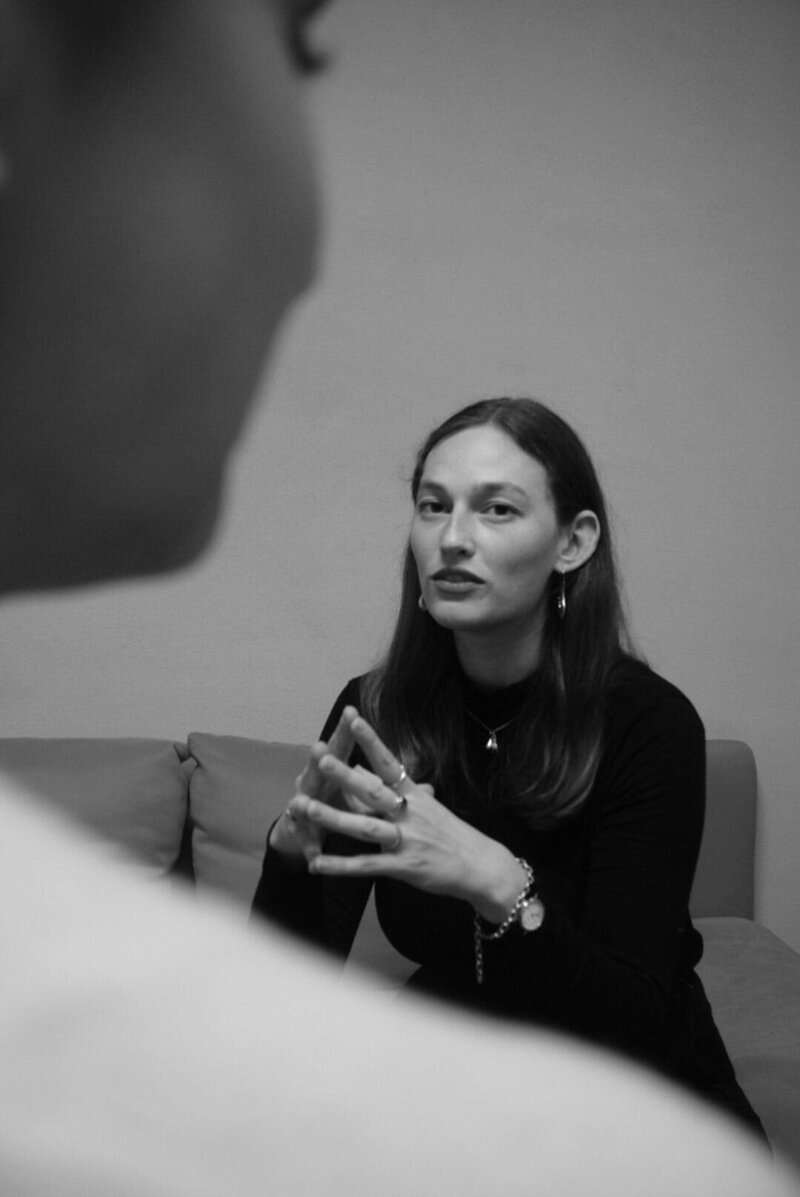 Thoughtful woman seated with hands clasped, gazing to the side.