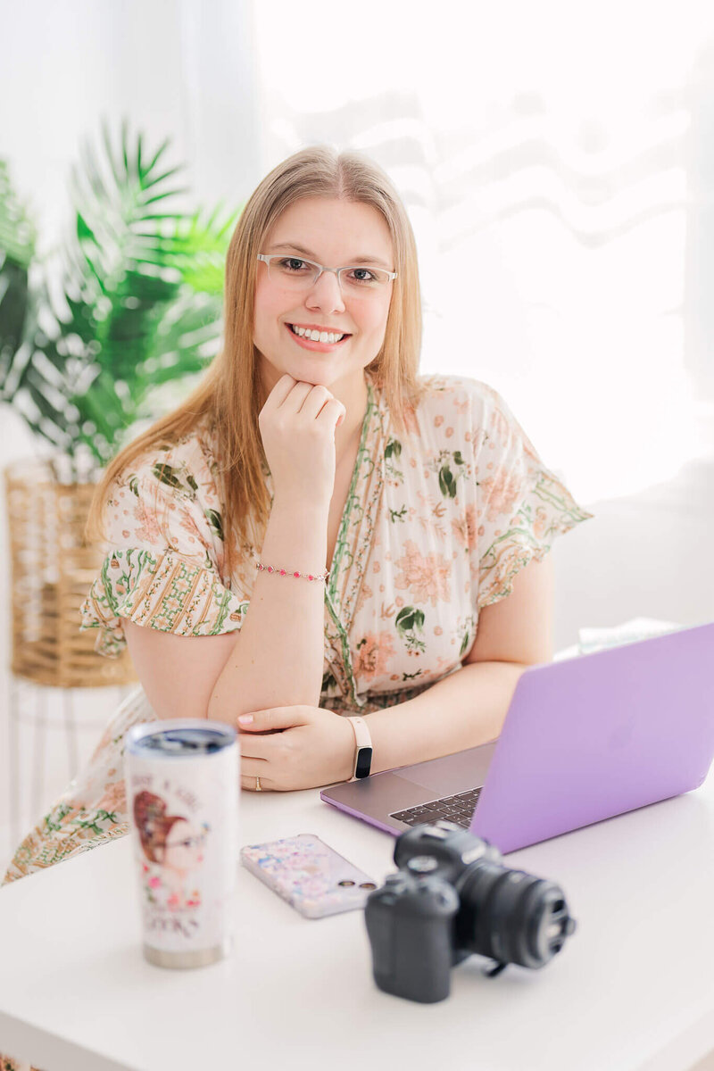 Northern Virginia photographer Melissa Driggers sitting at a desk and smiling at the camera.