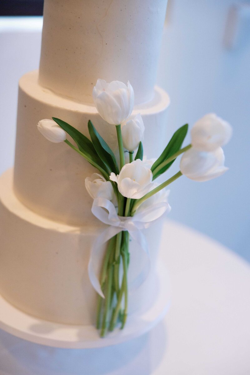White, three-tiered wedding cake decorated with while tulips.