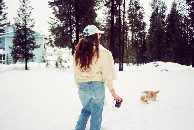 Eugene photographer, Heather, walks in the snow with her dog while holding a camera. 