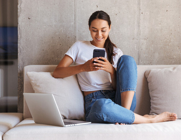 Woman learning from laptop and phone on sofa