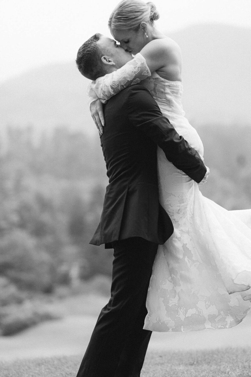 black and white bridal portrait, groom lifting bride up in the air