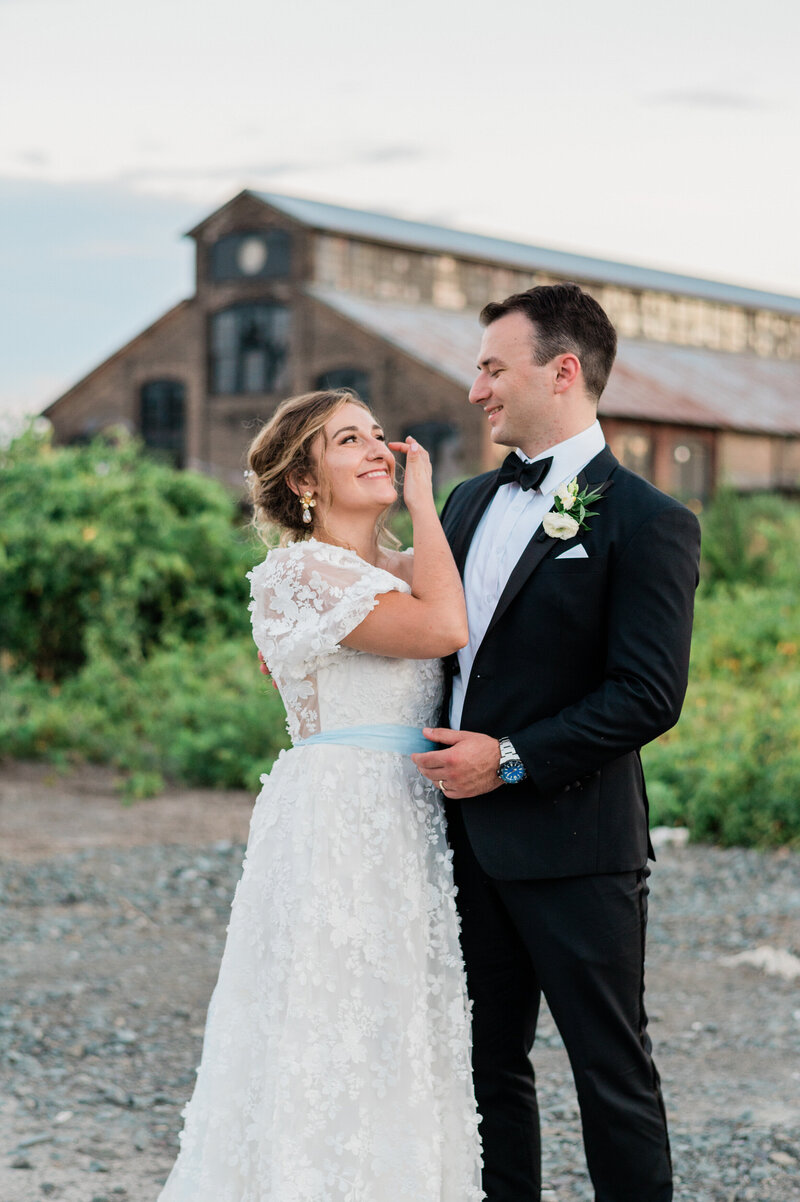 Bride moves hair from face while husband looks at her smiling