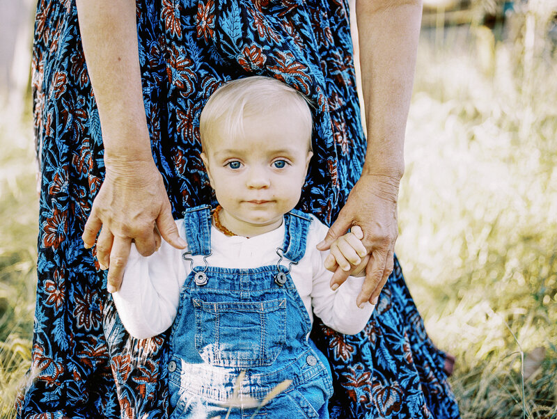 grandma holds up toddler in overalls