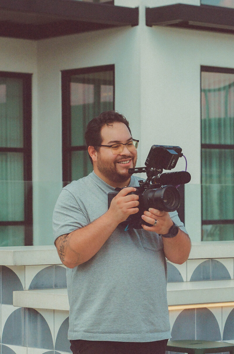 A man holds a camera and smiles.