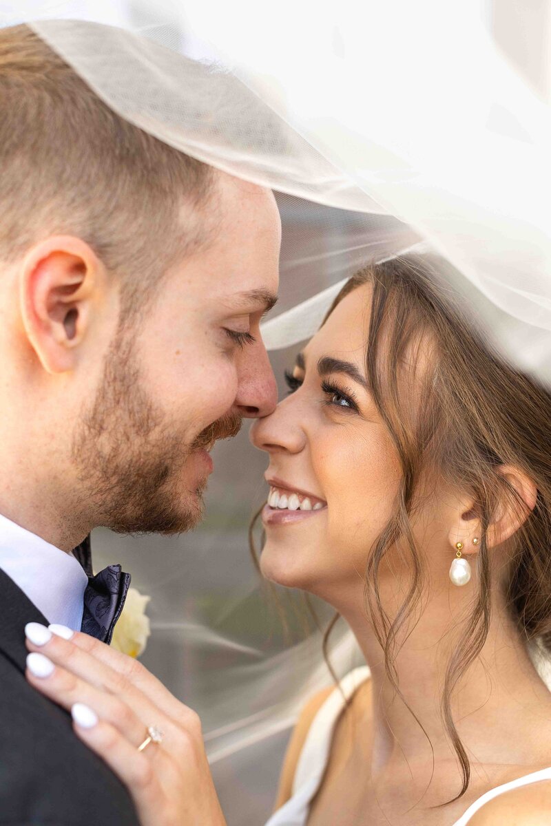 bride and groom under wedding veil smiling at each other