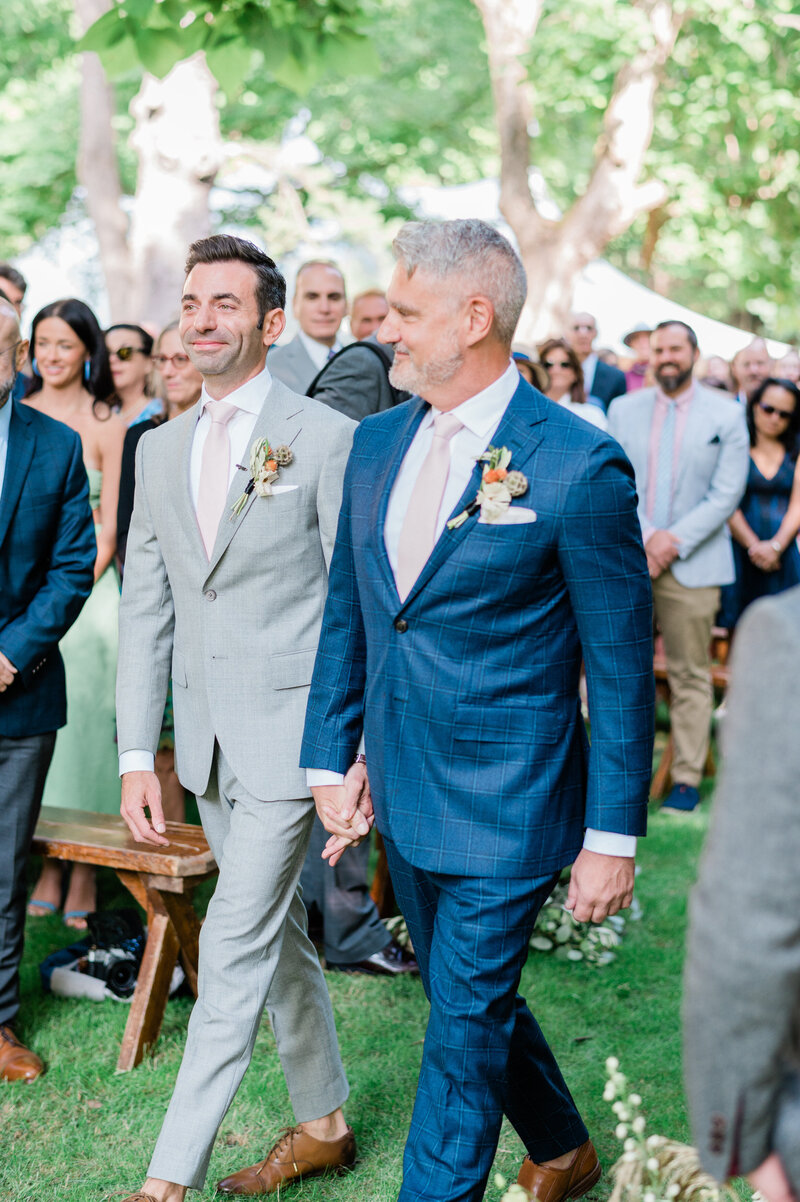 Two grooms at their Hudson Valley wedding walk down the aisle smiling 
