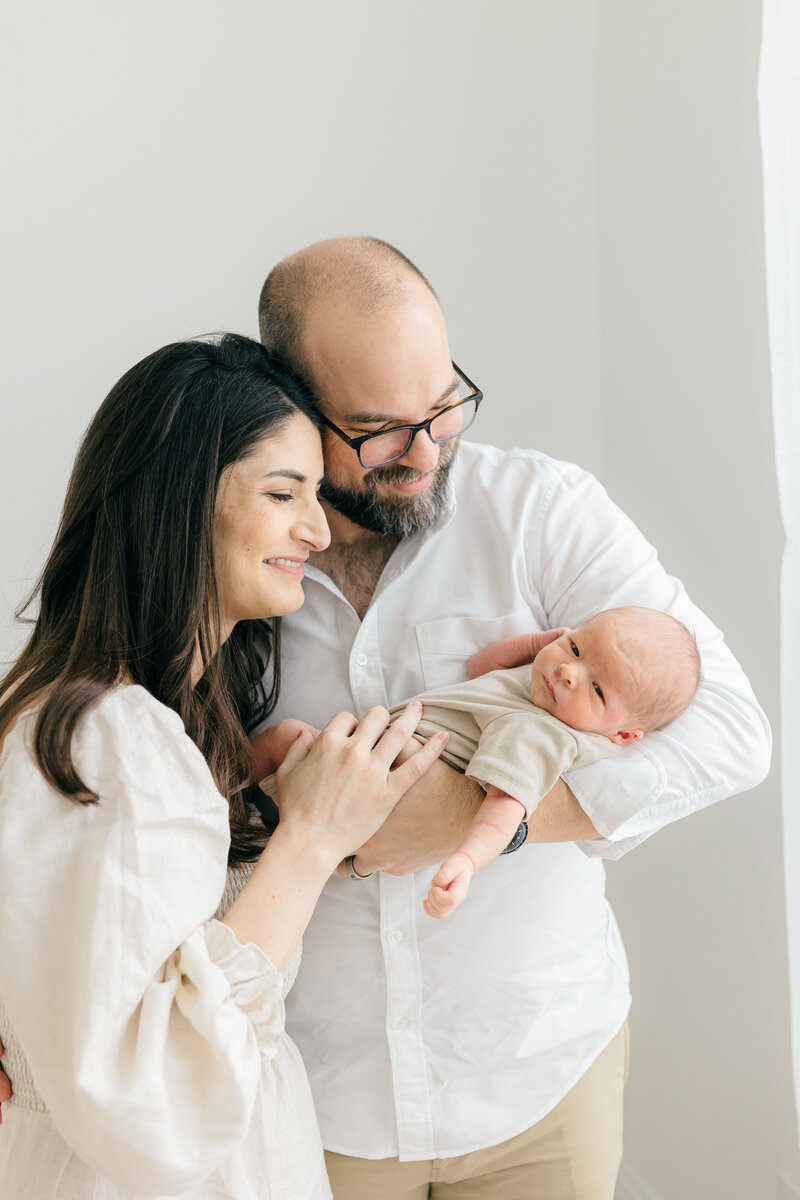 Couple embraces and lovingly smiles down at newborn baby boy during studio newborn photos with Alyson Teresa Photography in Tampa, Florida
