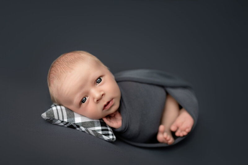 Curious eyes and soft wrap – a newborn boy in huck finn pose on dark grey.
