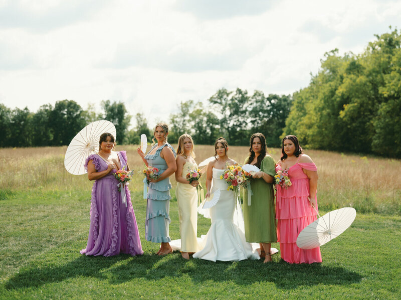 Bridal party posing with umbrellas at the forest edge before wedding cereony