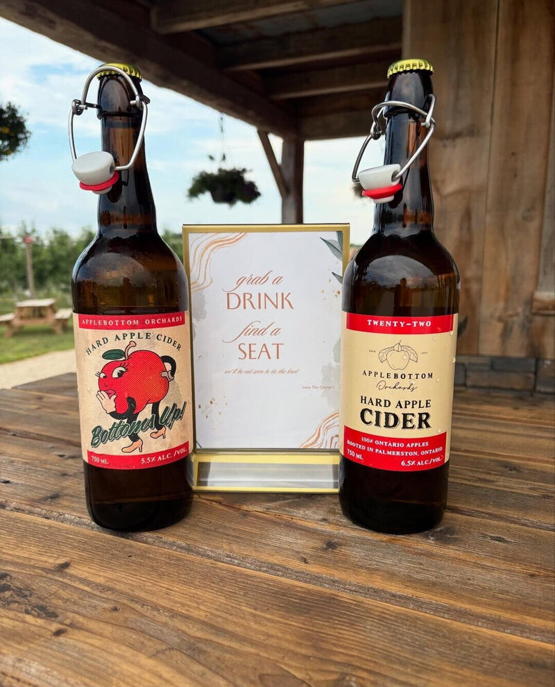 Two bottles of hard cider next to a sign at a wedding that took place at Applebottom Orchards.