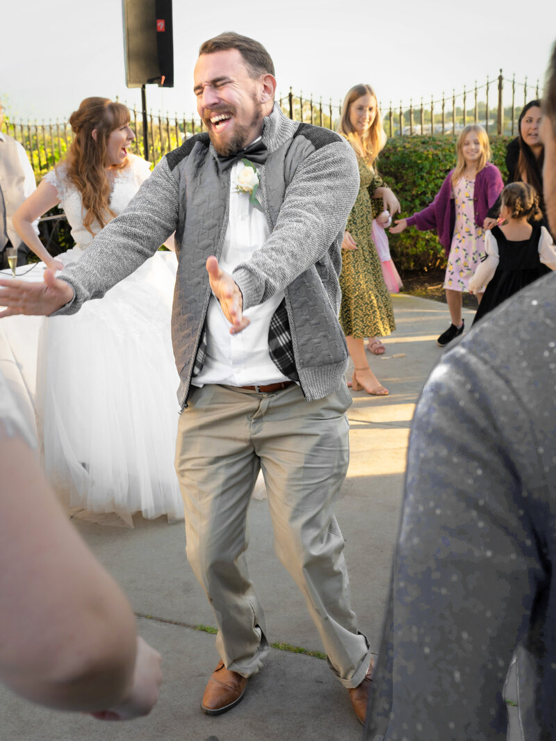 A groomsman's arms are held out straight in front of him in an exuberant dance move as he laughs with his eyes closed at an afternoon wedding reception. Photo by SAVI Photography - Los Angeles CA Photographer