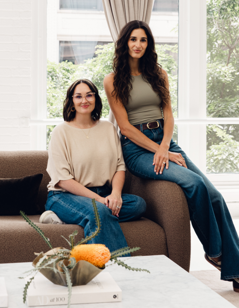 photo of two women sitting on a couch in a living room 