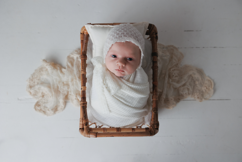 newborn-baby-in-white-wrap-and-bonnet-in-basket-white-floor