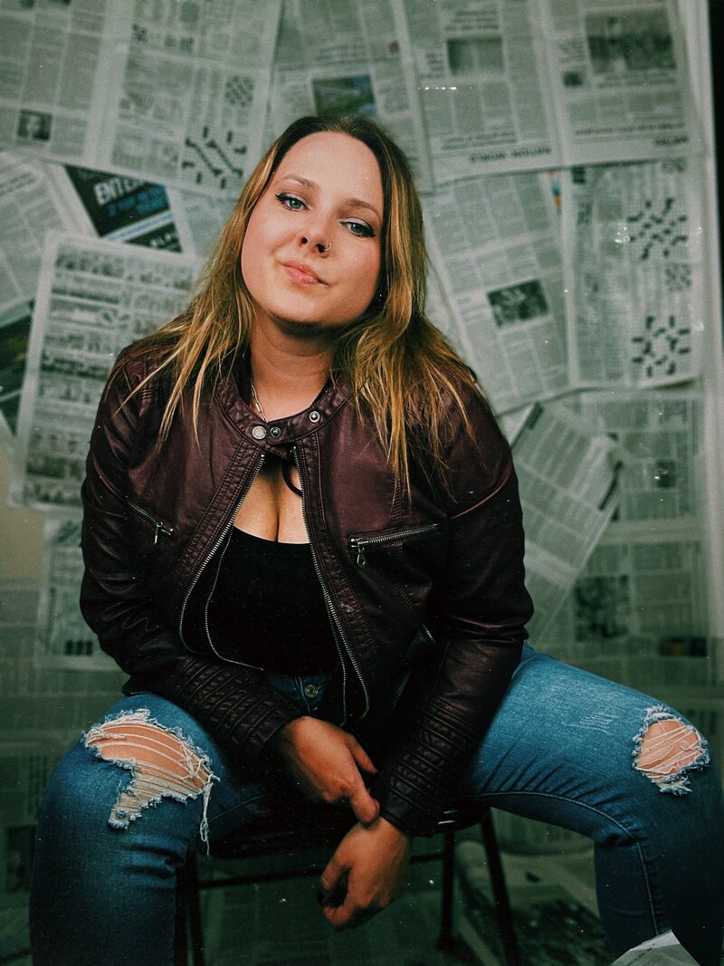 Photo of Kristina a life coach for women, sitting on a chair, leaning forward, with a newspaper backdrop behind her