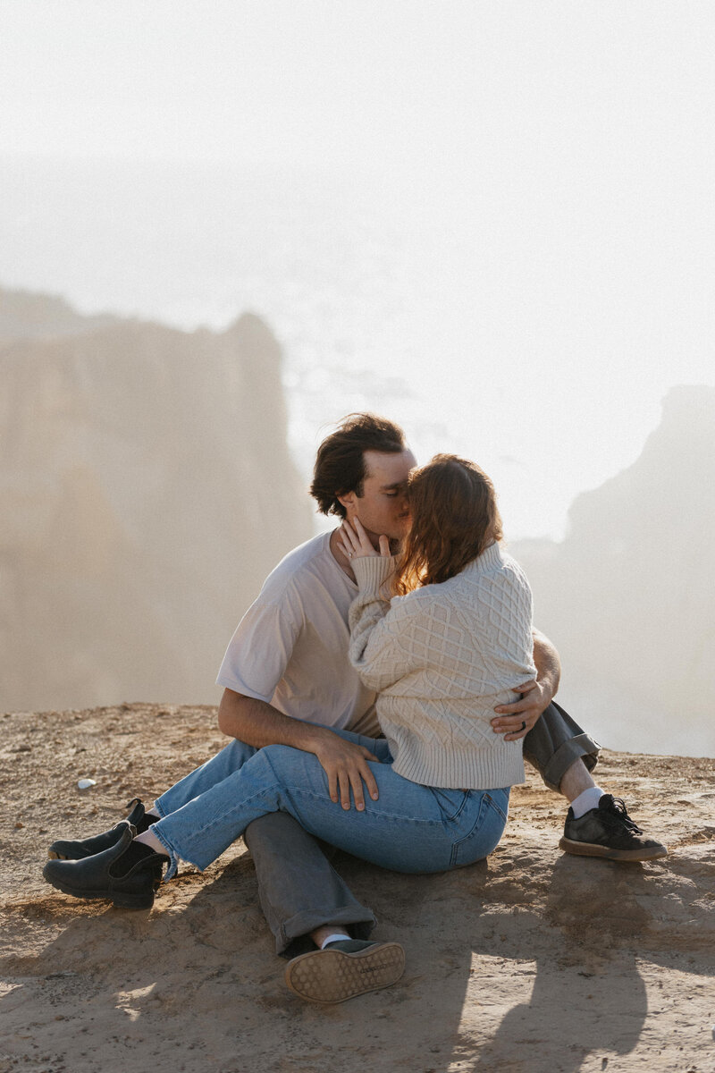 A couple sitting on a rock close together about to kiss 