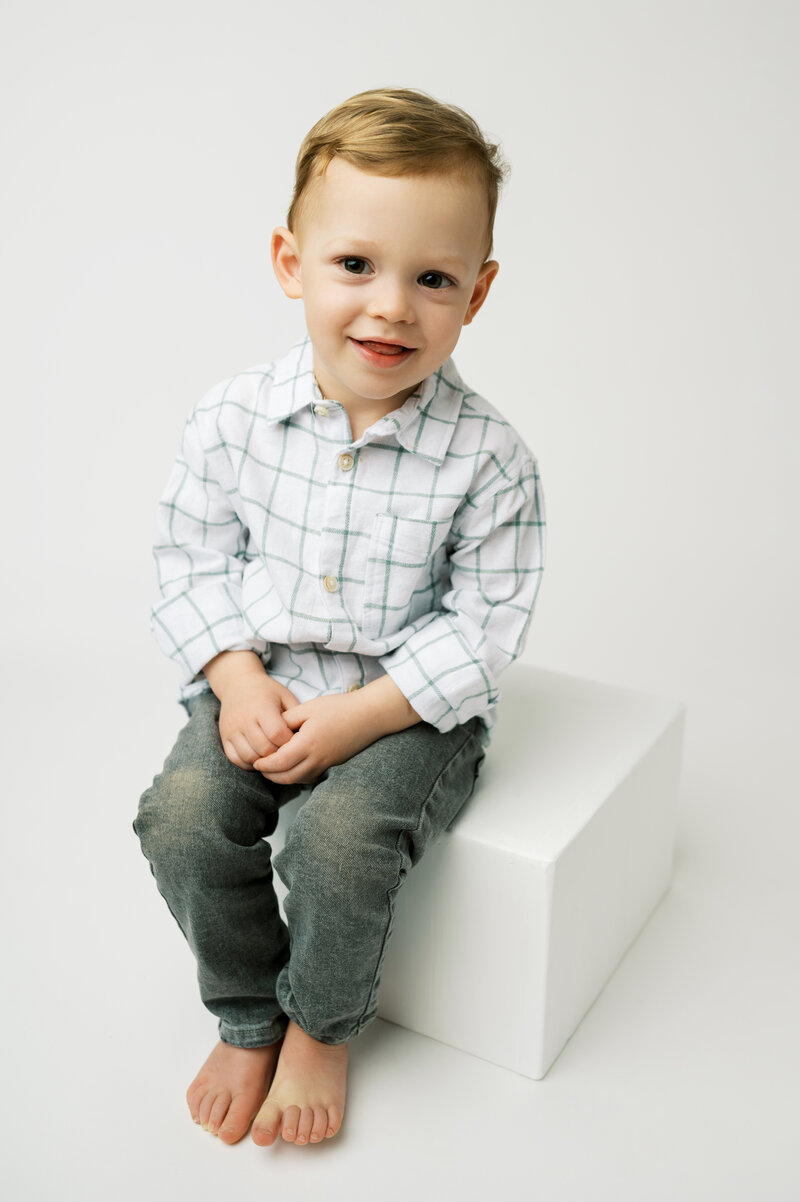 Little boy standing in front of a wooden bench grinning