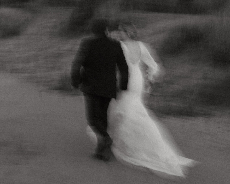 Black and white blurry photo of a couple running in their wedding clothes