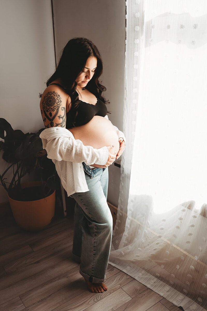 A momma to be embraces her growing baby belly during a relaxed and casual maternity session at the Bismarck, ND studio of Nikii Pix Photography.