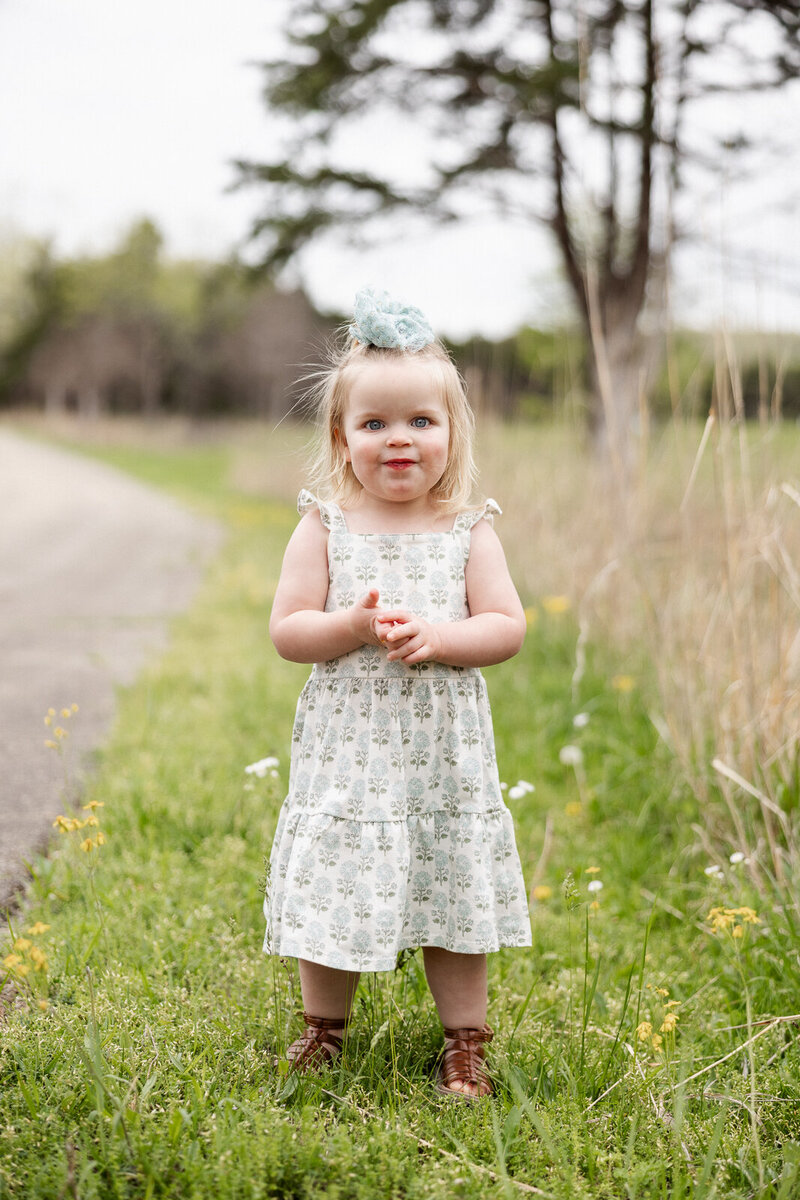 Portrait of a little girl standing in grass with flowers smiling at the camera taken in Bonne Terre, Missouri. 