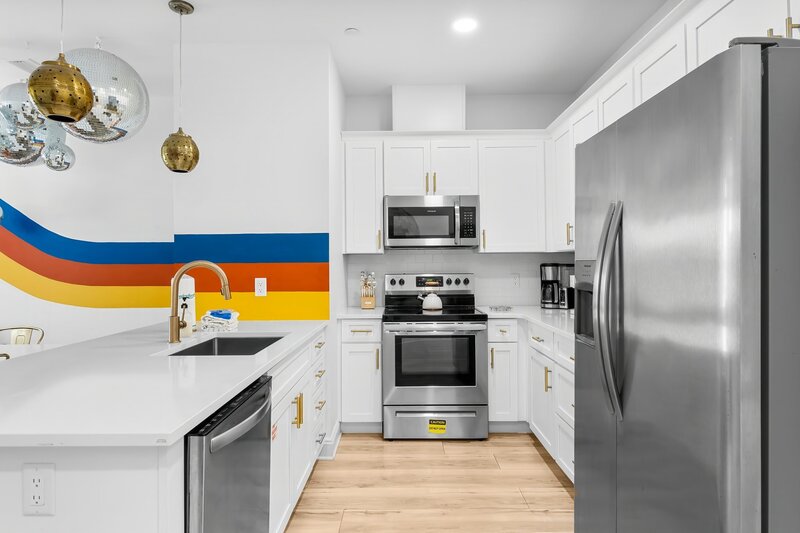 White cabinetry kitchen with stainless steel appliances and colorful striped accent wall, perfect for groups staying near Panama City Beach and Carillon