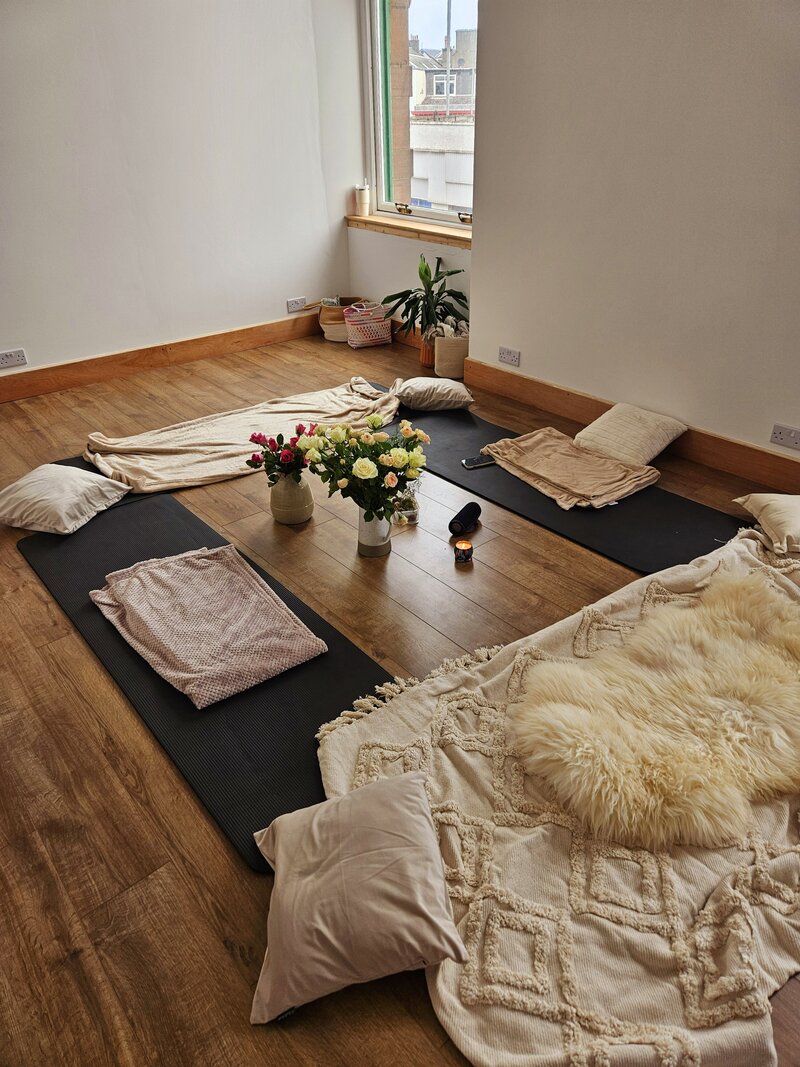 A studio space with yoga mats, blankets, cushions and flowers set up ready to host a workshop.
