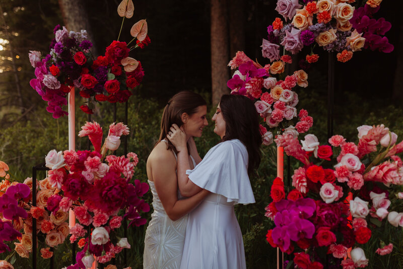 Two lesbian brides stand in front of a luxurious wedding altar with contemporary bright tropical floral designs in Forks, Washington