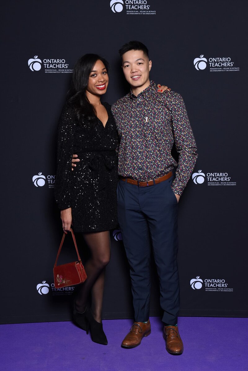 A stylish couple posing at the Ontario Teachers' event, standing on a purple carpet with a branded backdrop, showcasing professional event photography