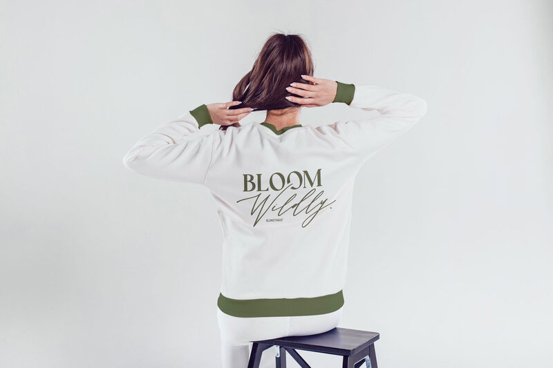A model wearing a sweatshirt with her back to the camera showing 'Bloom Wildly' designed by Blomsthaus.