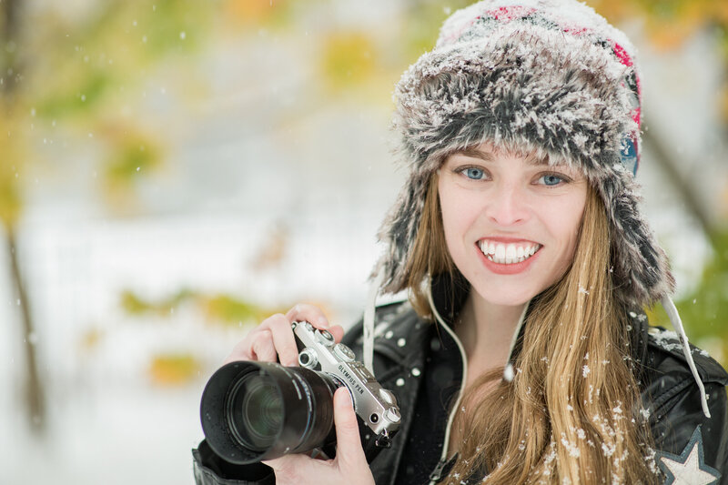 Jen Stitt holding her camera in a snowy landscape, showcasing her passion for capturing breathtaking engagement session moments in unique and magical settings.