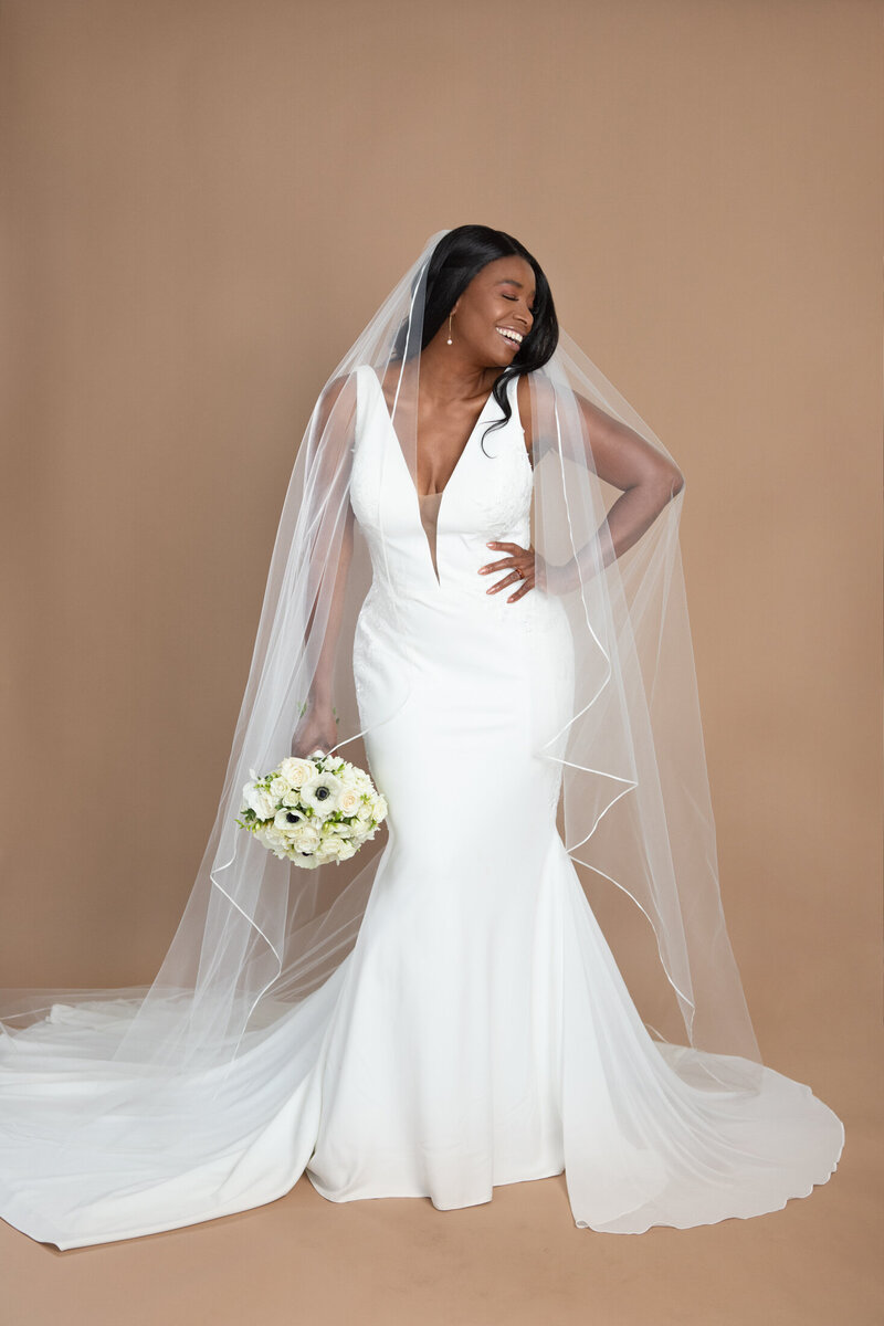 Bride wearing a cathedral length ribbon edged waterfall veil and holding a white and black bouquet