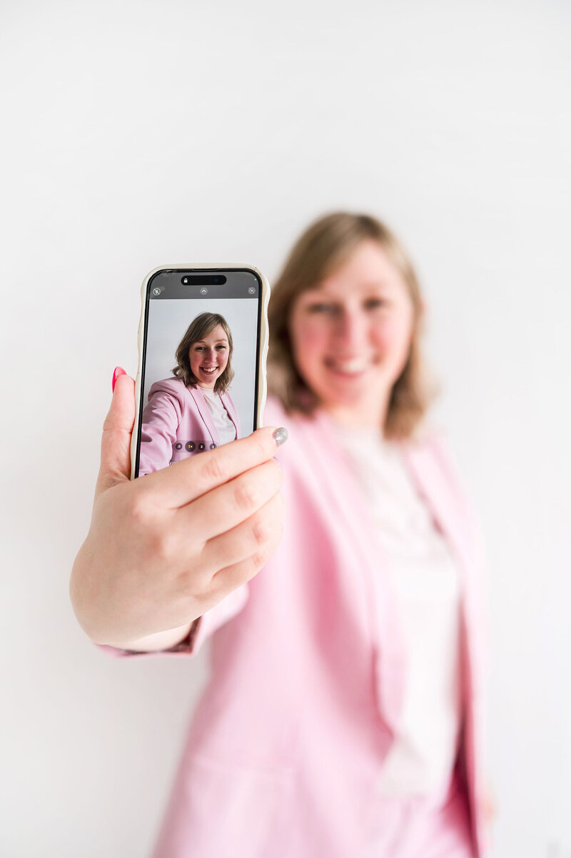 Kat Murphy in a pink blazer taking a selfie with her iphone