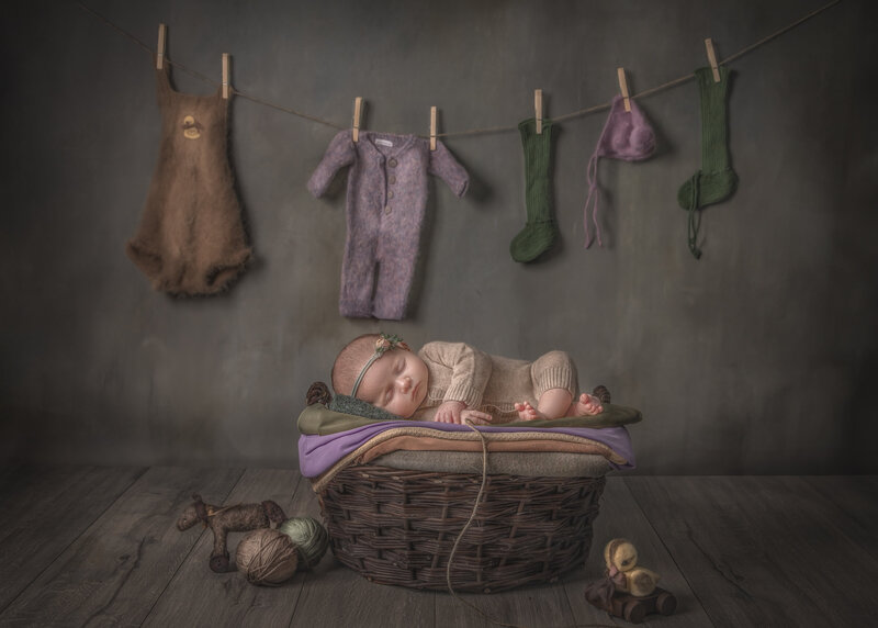 "Newborn baby peacefully sleeping in a custom laundry basket with tiny baby clothes hanging, captured in a charming and whimsical fine art photography session in Ottawa."
