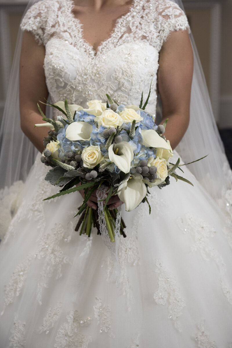 A bride shows off her blue and cream wedding bouquet at her winter wedding.