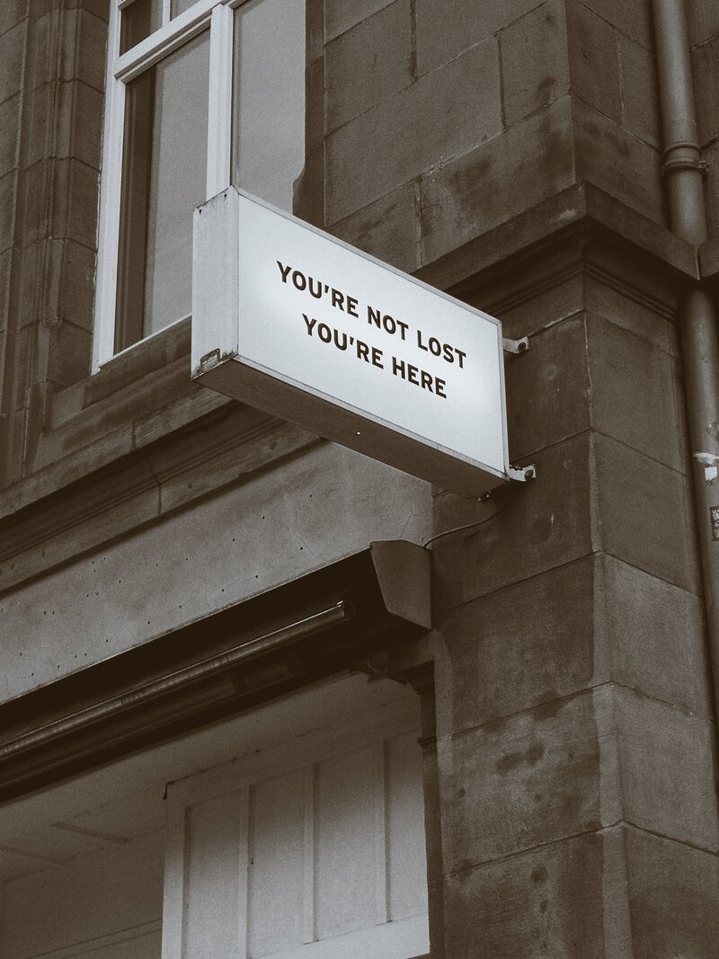 A grey building has a large sign that says, You're not lost, You're here.