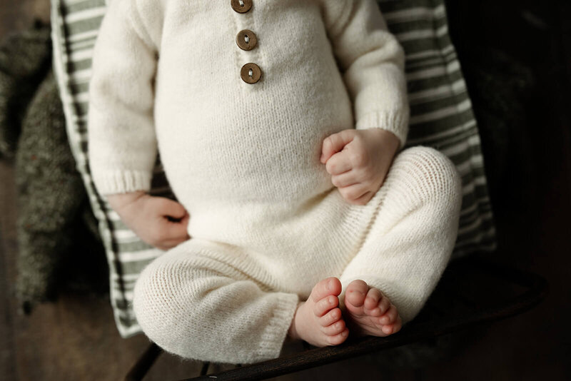 A serene newborn baby is sleeping, wrapped snugly in a soft, neutral-toned fabric. The baby has closed eyes and a calm expression, lying against a gentle, textured backdrop that enhances the cozy atmosphere.