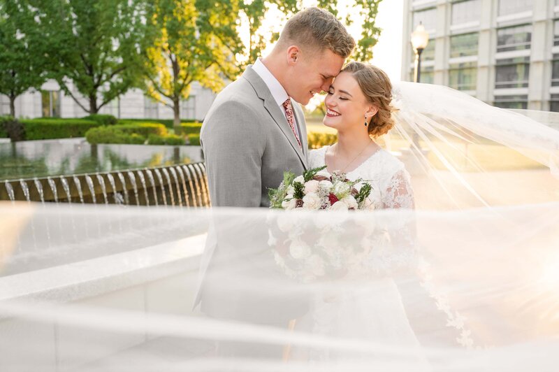 Bride and groom share a moment at the Utah State Capitol during wedding session, while wrapped in a long veil.