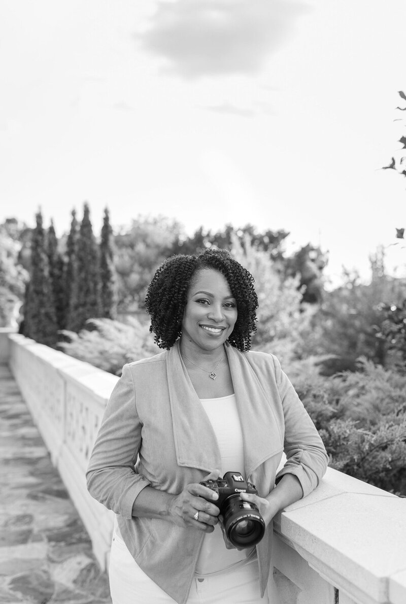 Lisa Yvette, professional photographer, smiling and holding a camera during an outdoor photoshoot.