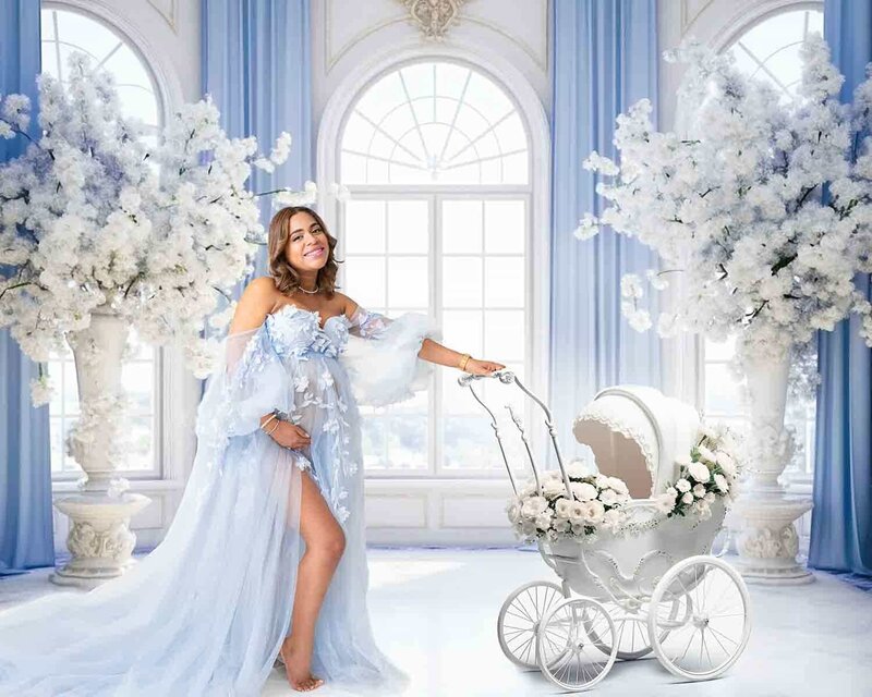 Pregnant woman in light blue gown posing with vintage white stroller surrounded by white florals in Birmingham studio – Winter Book the Look maternity session