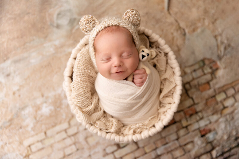 newborn girl with a big smile and closed eyes posed in the studio with a headband