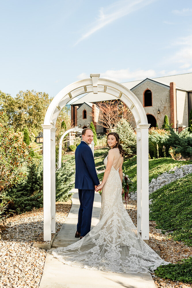 Erin and Stephen under white archway, looking back over their shoulders with big smiles