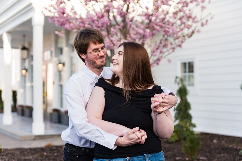 Couple holding hands near the lake at Canandaigua Lake House under blooming cherry trees.