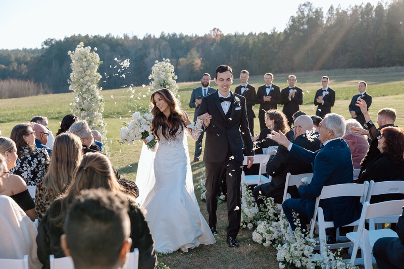 Bride and bridesmaids walk through a field laughing at one another